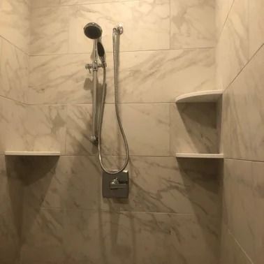 Shower with white marble-like tile, handheld showerhead, two built-in shelves.