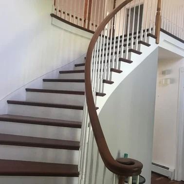 Curved wooden staircase with white balusters and brown handrail.