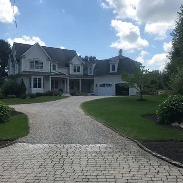 White house with a curved driveway, green lawn, and blue sky.