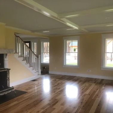 Empty room with wood floors, yellow walls, white trim and coffered ceiling, staircase, and fireplace.