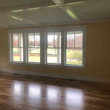 Living room with three windows overlooking a green lawn, hardwood floor, yellow walls, and a coffered ceiling.
