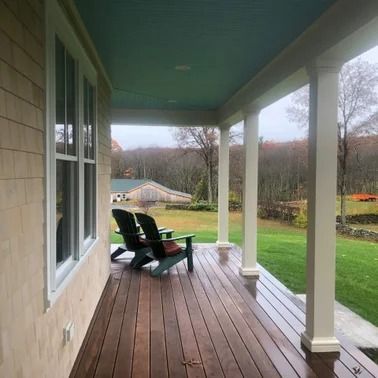 Wooden porch with Adirondack chairs, overlooking a grassy yard and distant barn. Turquoise ceiling.