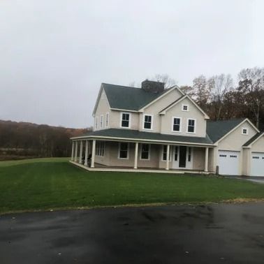 Two-story beige house with a porch and attached garage on a green lawn under a cloudy sky.