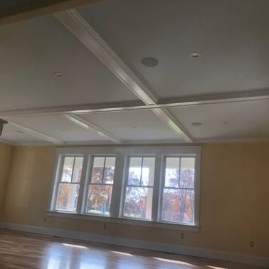 Interior view of a room with a coffered ceiling, windows, and light yellow walls.