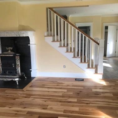 A wood floor leads to a staircase with white balusters. A fireplace is to the left.