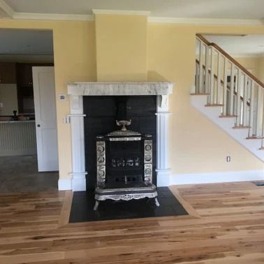 Fireplace with a black stove in a room with hardwood floors and stairs.