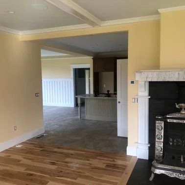 Interior view of a house with wooden floors, yellow walls, and a fireplace. An open doorway leads to another room.