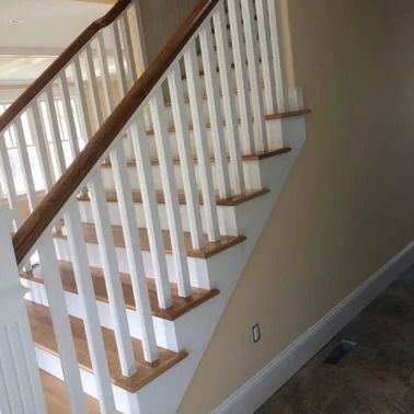 Staircase with white balusters and wooden handrail and treads, next to a beige wall.