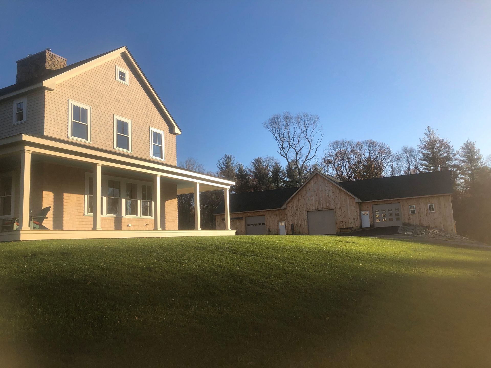 Beige farmhouse with a wraparound porch and an attached barn on a sunny day.