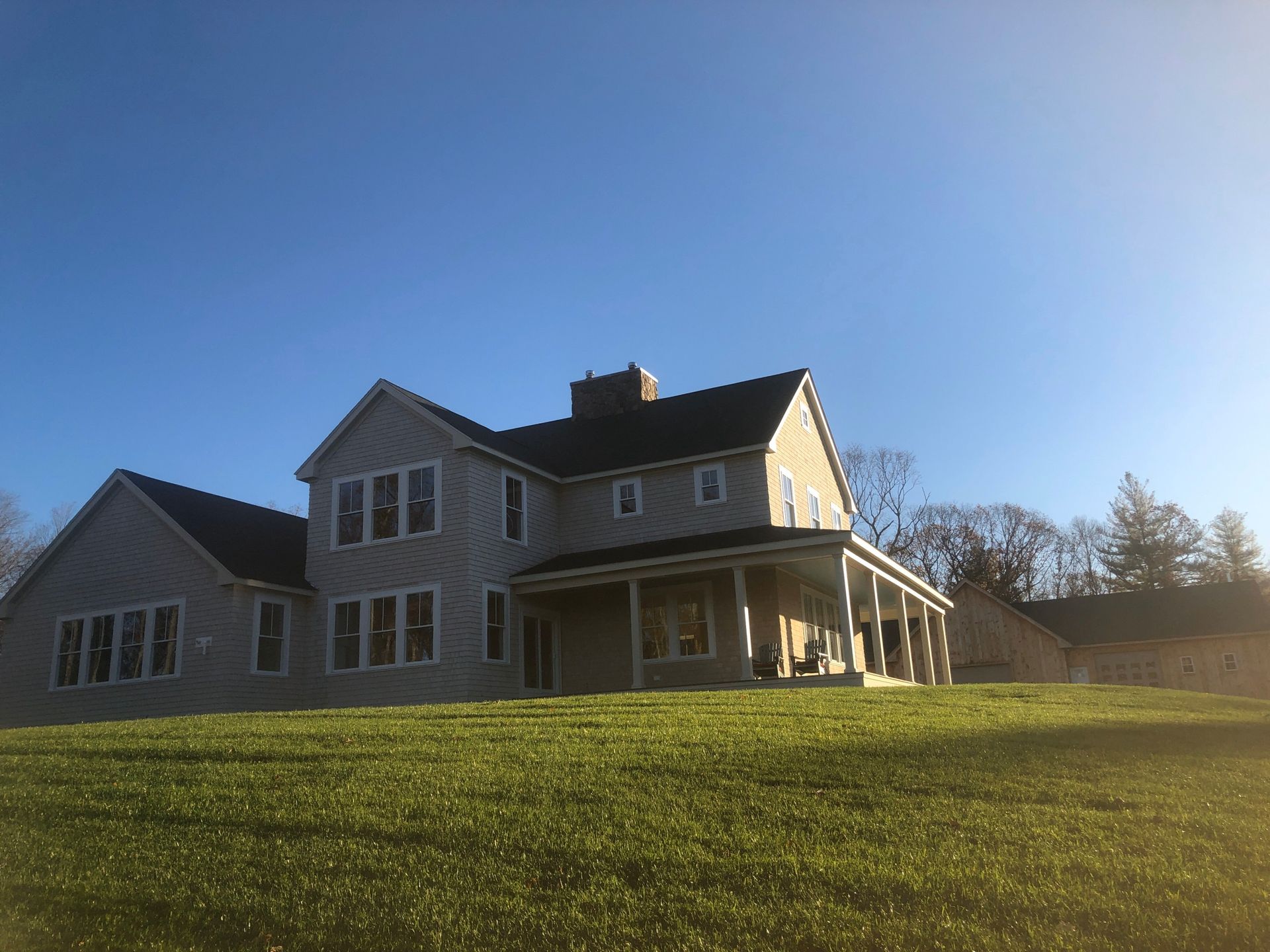 Large two-story house with a wrap-around porch and a green lawn under a clear blue sky.