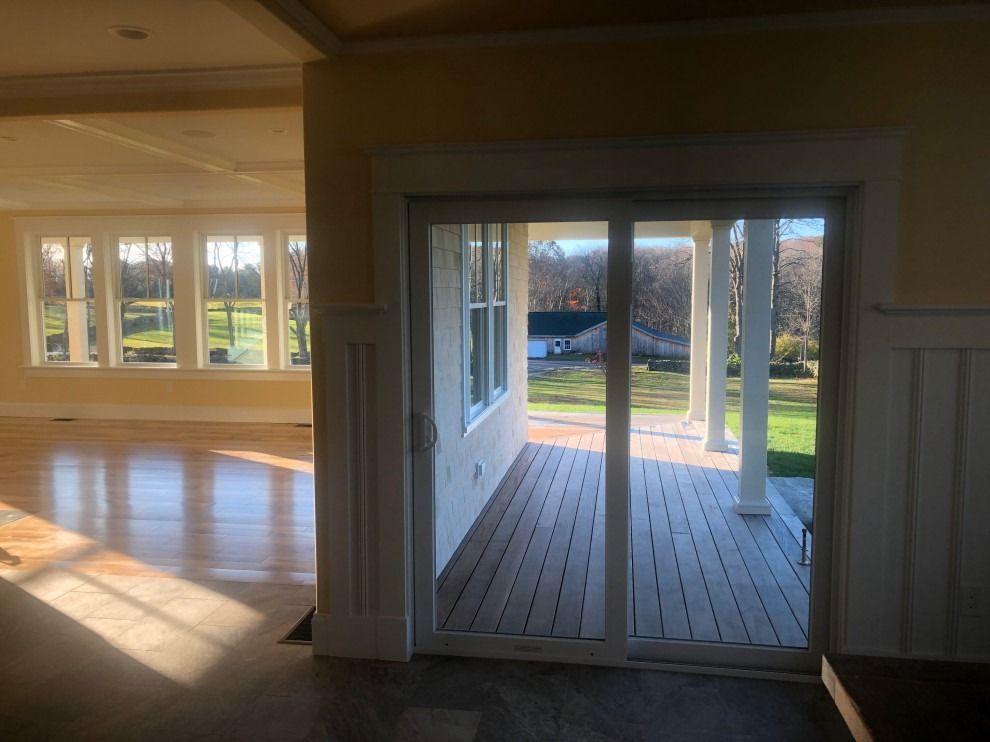 Sliding glass door opens to a porch with columns. Sunlight streams in, illuminating the interior of a home with hardwood floors.