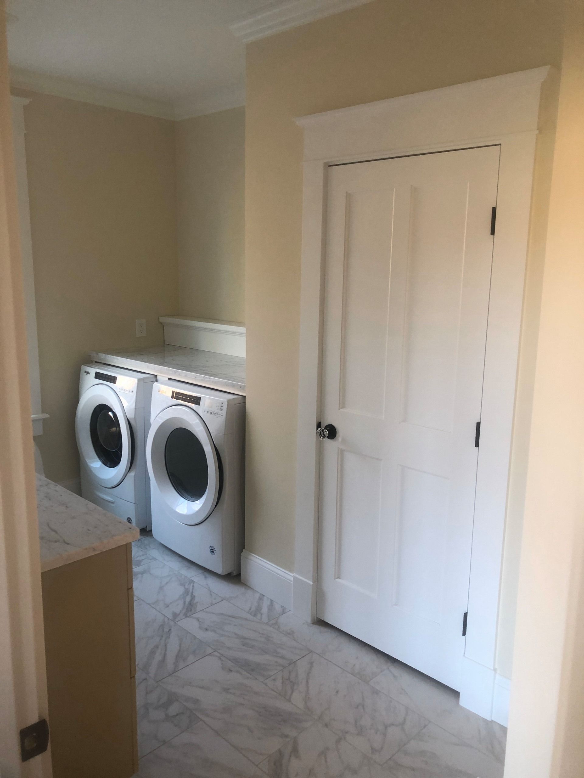 Laundry room with white washer and dryer, white door, and marble floor.