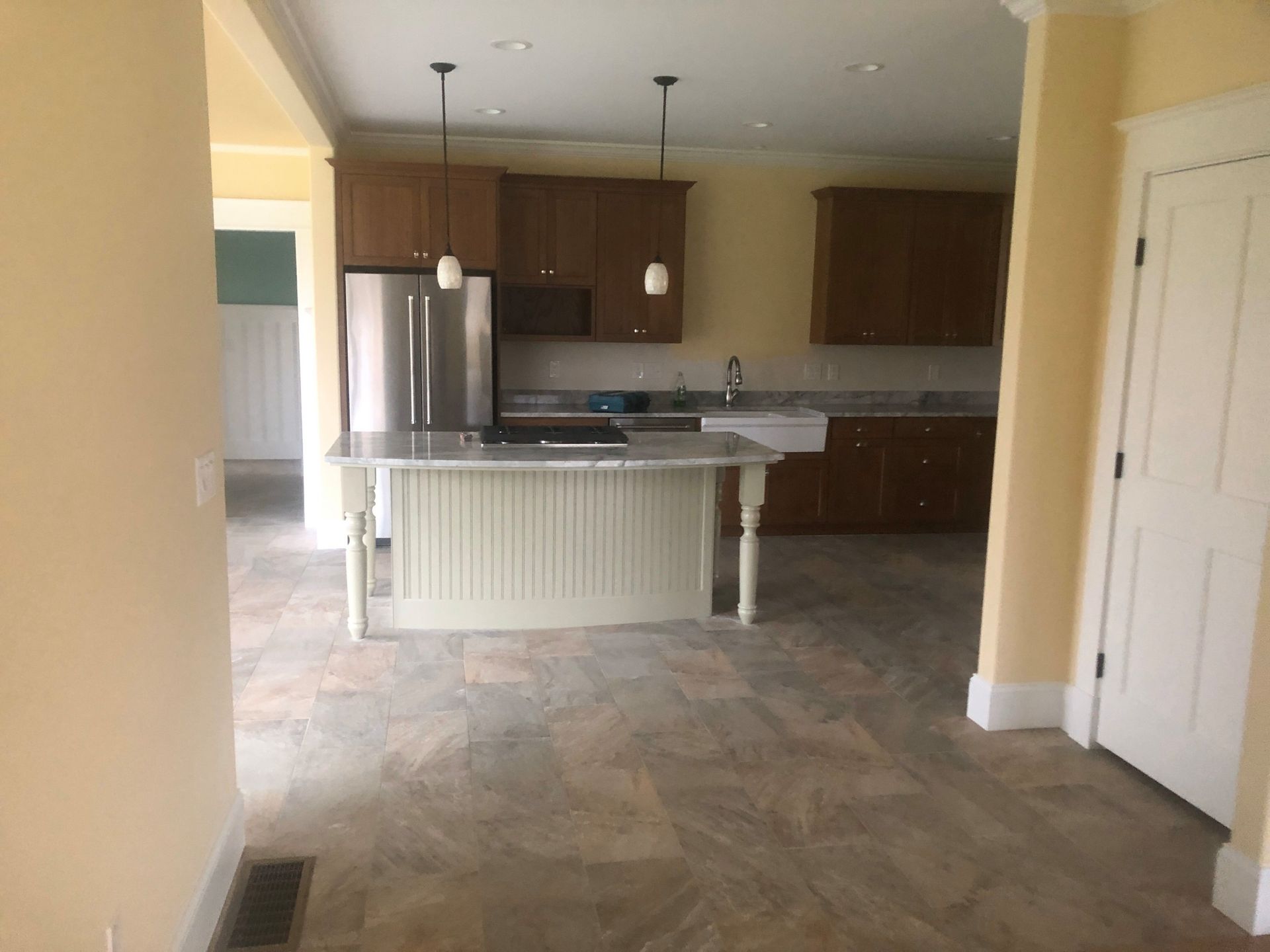 Kitchen with brown cabinets, white island, and stainless steel appliances. Beige walls and tiled floor.