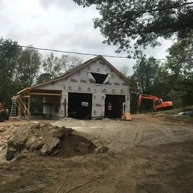 Garage under construction with two bays, excavator, and dirt pile.