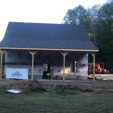 Construction of a building with a dark roof and a covered porch.