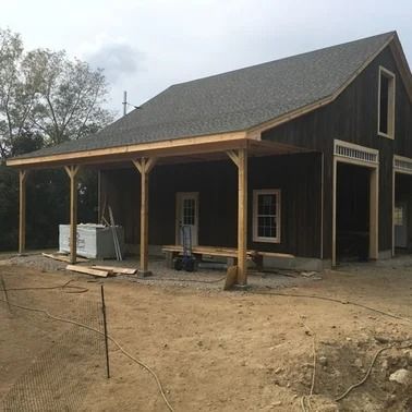 Brown barn-style building with a porch, under construction on a dirt lot.
