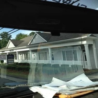 Exterior of a light blue building with a white porch. The view is from inside a car.