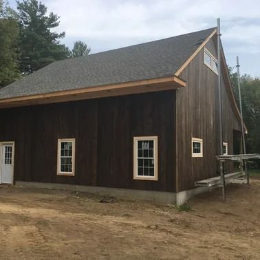 Brown wooden building with light window frames and a gray roof, in a rural setting.
