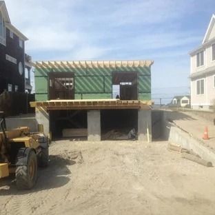 Construction site: building with open framing, two garage bays, yellow front-end loader, sandy ground.