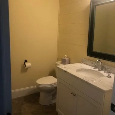Small bathroom with a toilet, sink, and mirror. Beige walls, white vanity, black mirror frame.