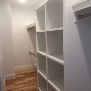 Empty white walk-in closet with built-in shelving and wooden floor.
