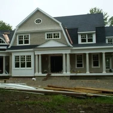 New house under construction with light-colored siding, black roof, white trim, and porch columns.