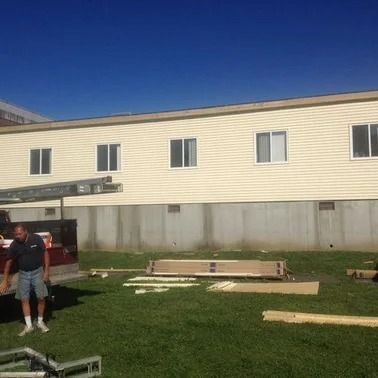 Man stands near building with construction materials on green grass under blue sky.