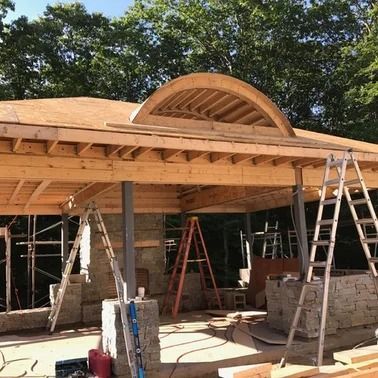 Construction of a building with wooden beams, stone pillars, and arched roof detail; ladders and tools visible.