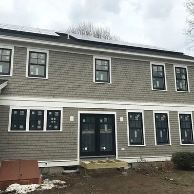 Two-story house with gray shingles, black framed windows, and solar panels on roof.