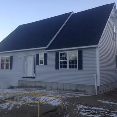 Gray house with black roof, blue shutters, and construction barrier.