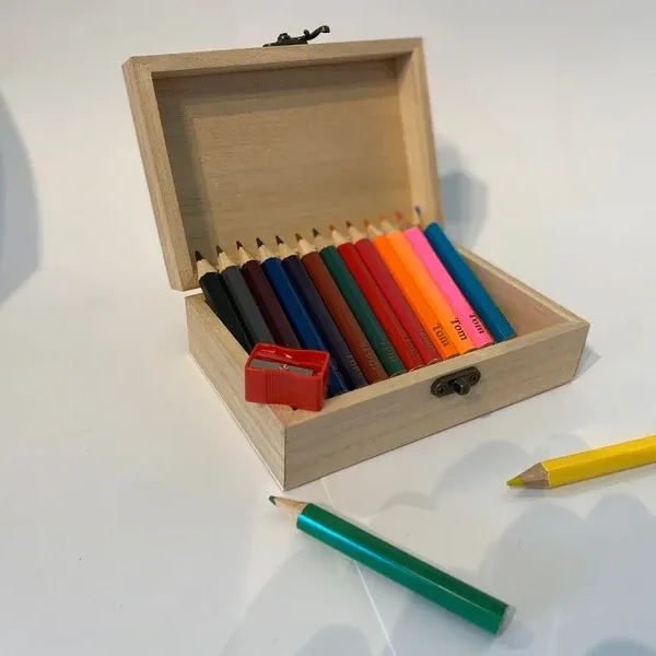 Een open houten doos met kleurpotloden op een witte ondergrond, met een paar potloden eromheen verspreid.