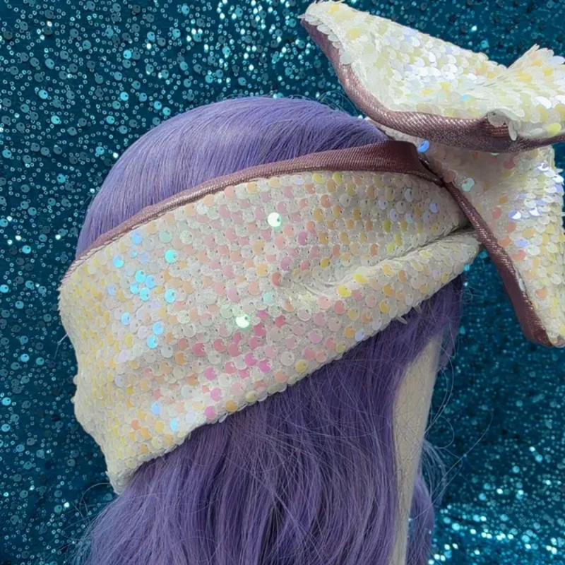 Haaraccessoire met een grote mauve strik en een witte strik met stippen op een blauwe glitterachtergrond.