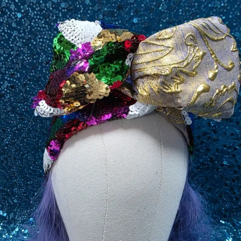 Mannequinhoofd met een kleurrijke paillettenstrik en een zilverkleurige,met goud geborduurde strik op een blauwe achtergrond.