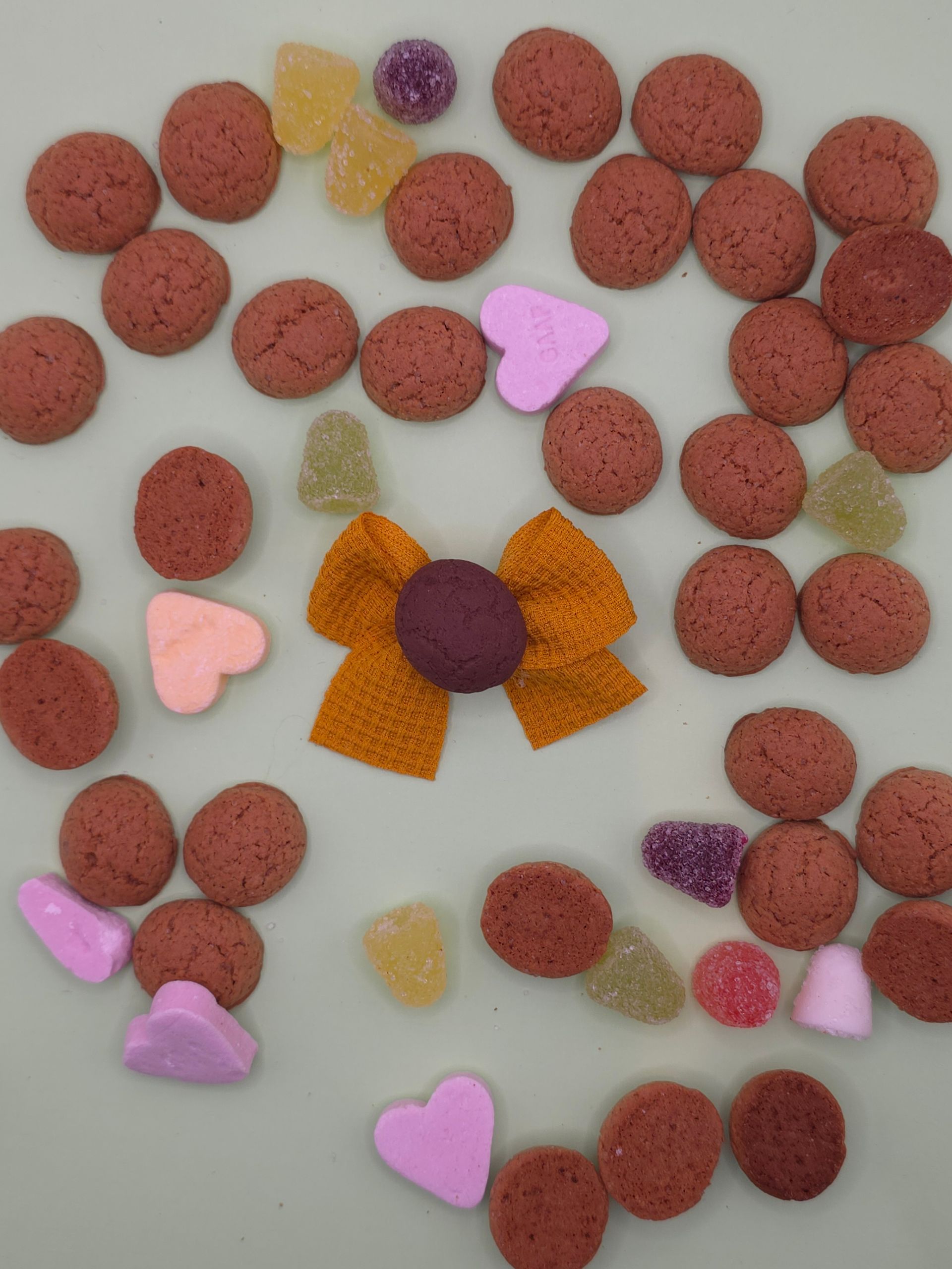 Verspreide roze koekjes met kleurrijke hagelslag rond een paars midden op een witte ondergrond.