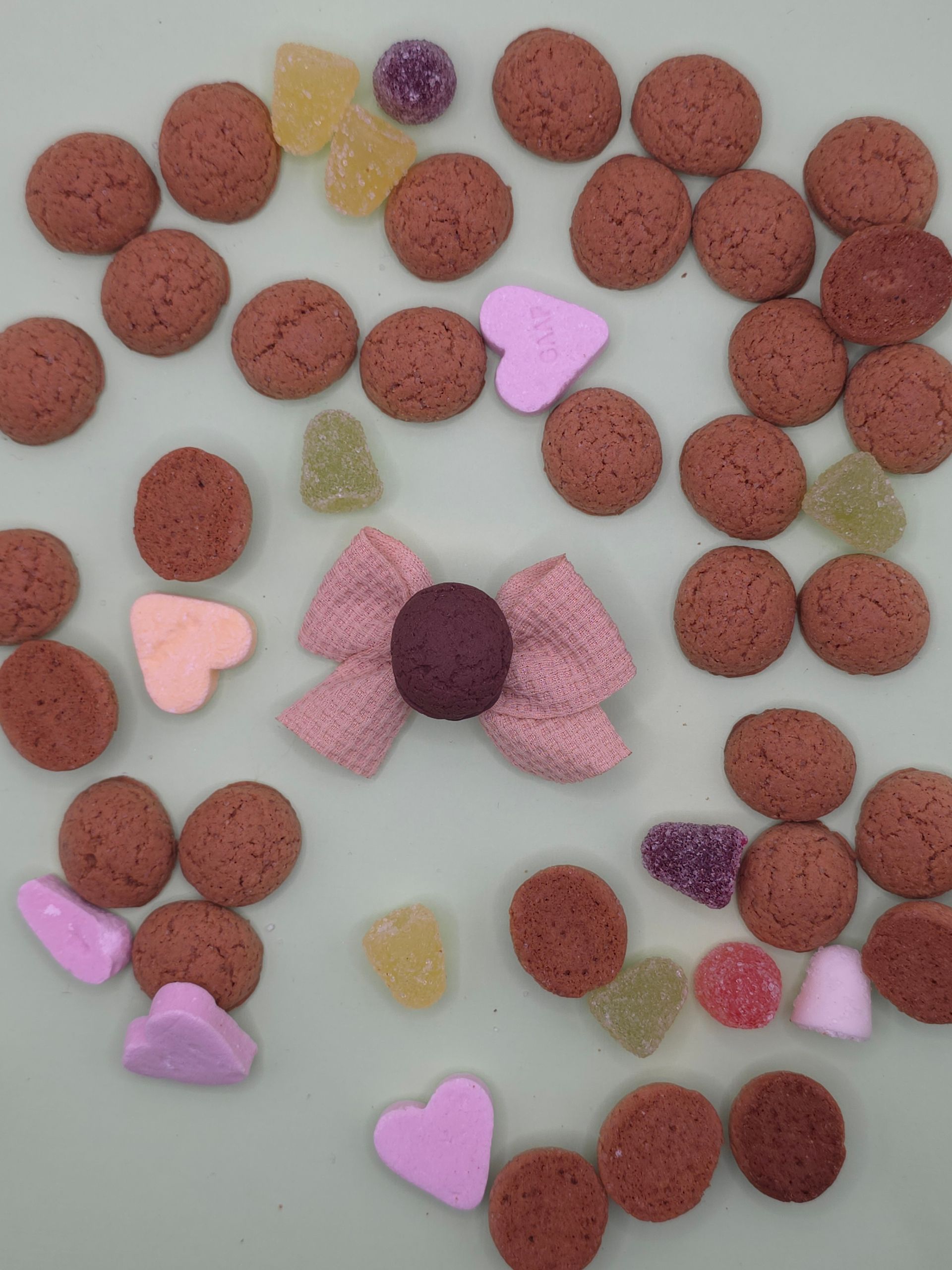 Hartvormige snoep- en koekjesschikking met roze, paarse en bruine snoepjes op een lichte ondergrond.