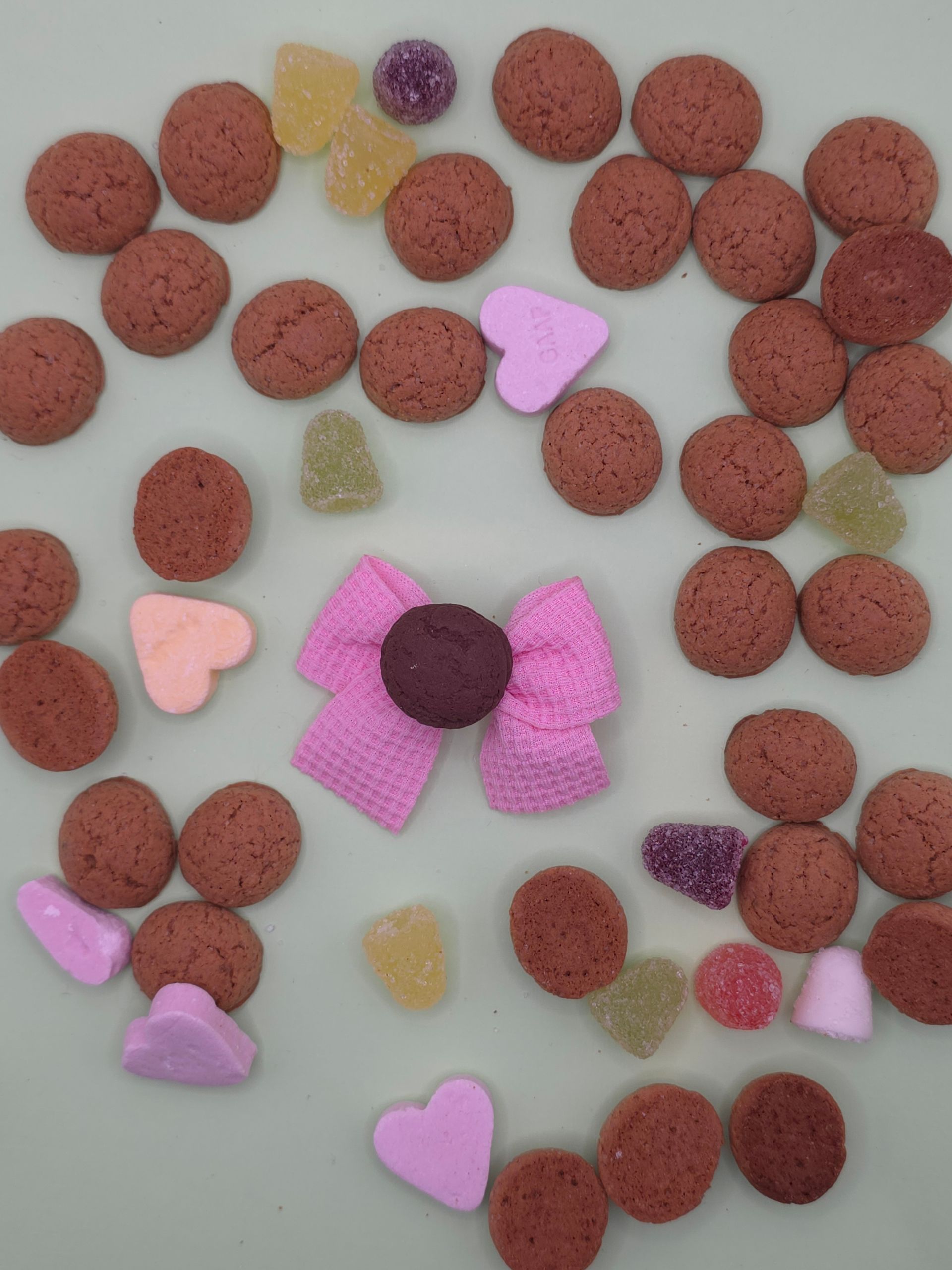 Verspreid rood brokjesmateriaal en kleurrijke hartvormige snoepjes rond een roze hart met een bruin midden.