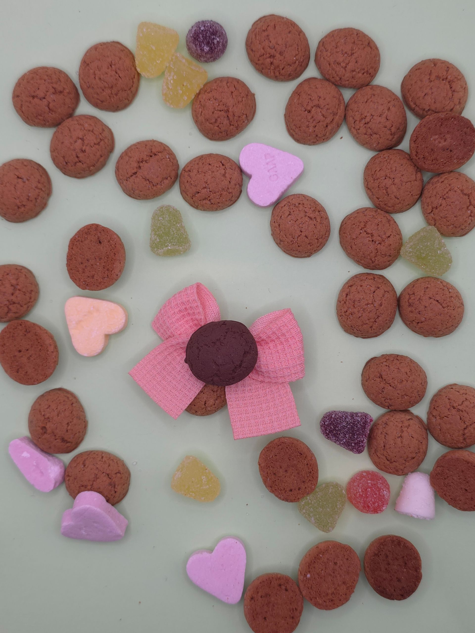 Verspreide rode cornflakes en kleine pastelkleurige snoephartjes op een lichte ondergrond vormen een losse bloemvorm.