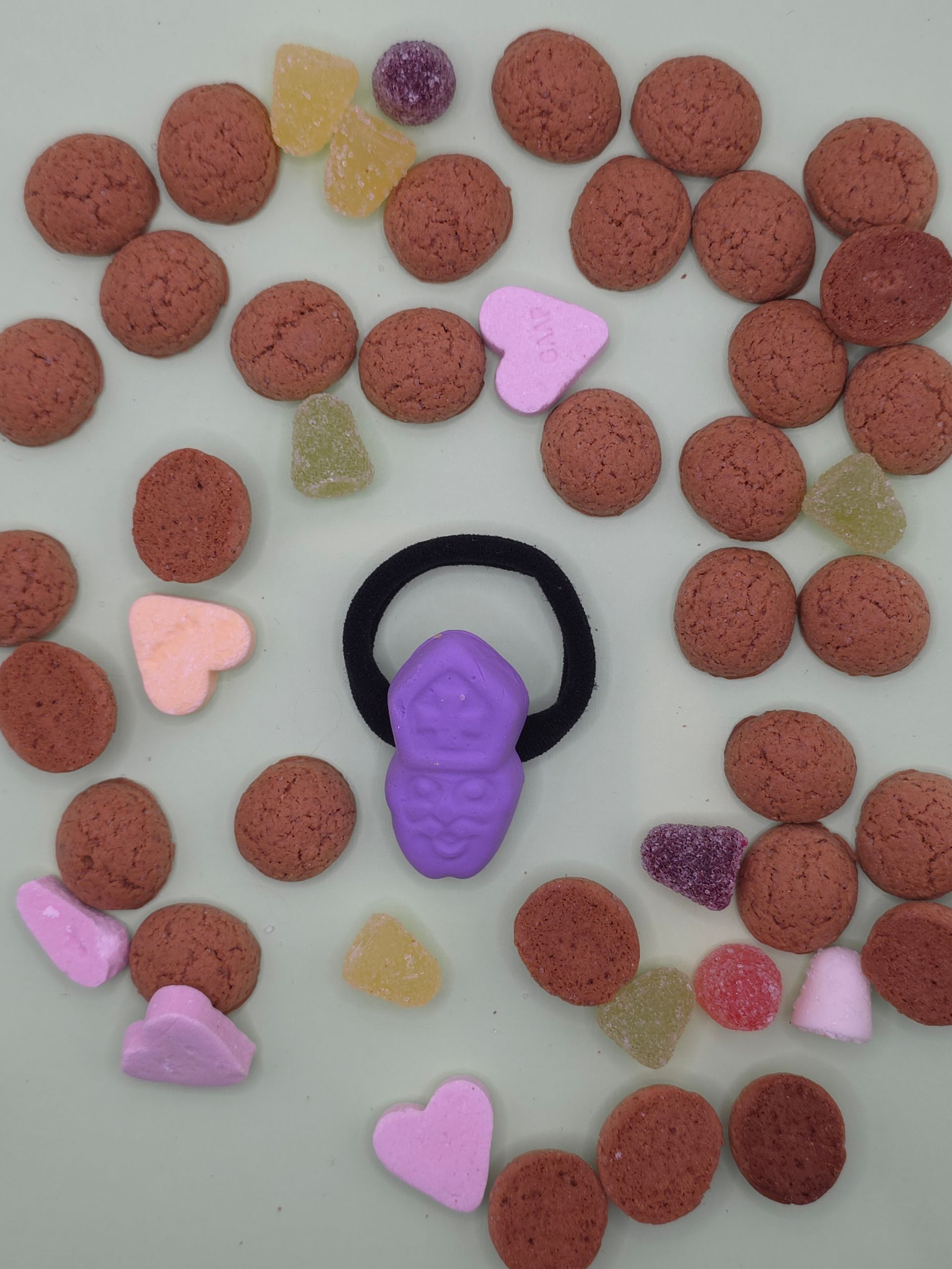 Paars bijvormig speeltje op een ring, omringd door verspreide rode en pastelkleurige kralen op een lichte achtergrond.