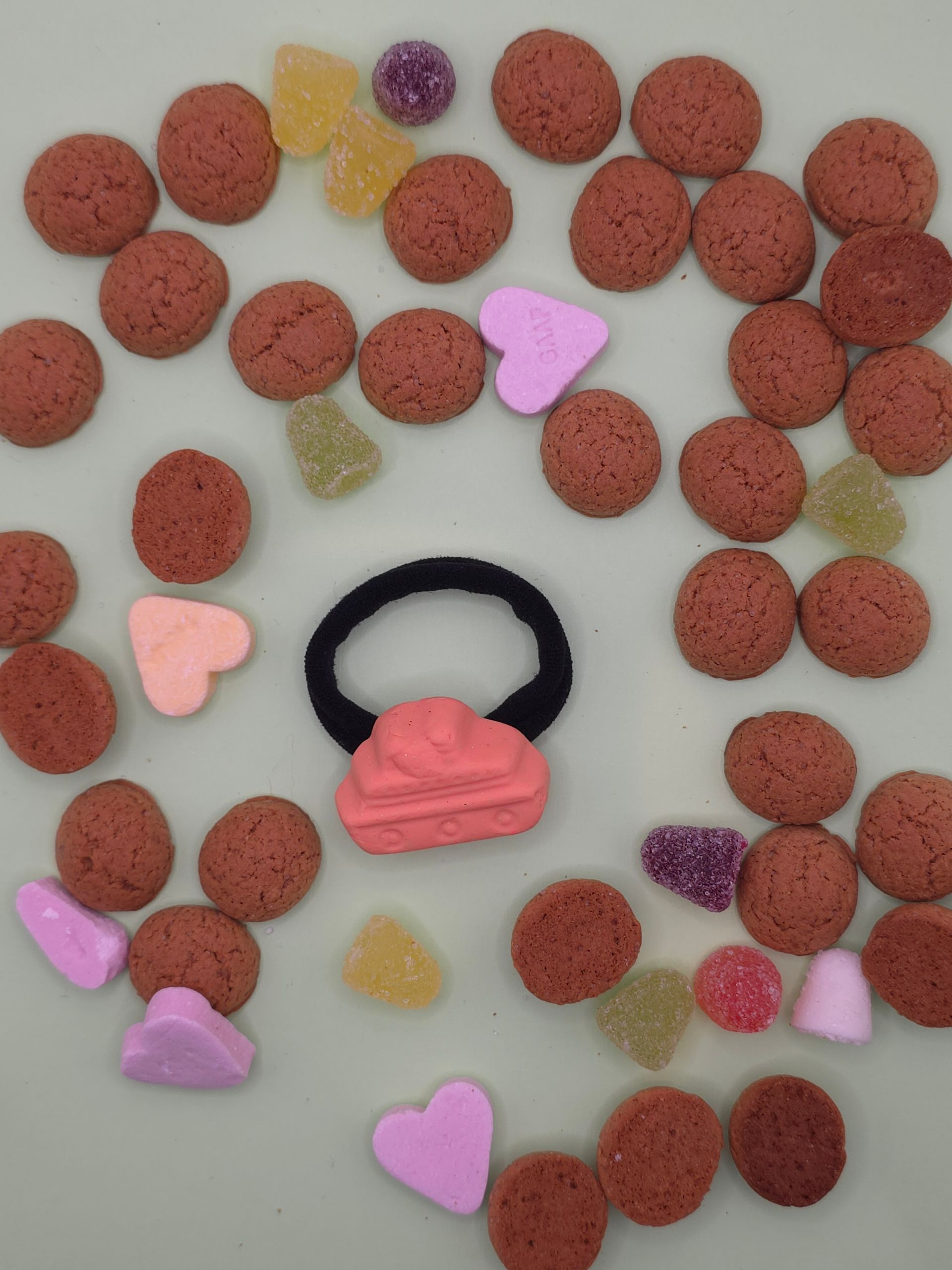 Verspreide bruine ontbijtgranenstukjes rondom roze en paarse hartvormige snoepjes op een lichte ondergrond.