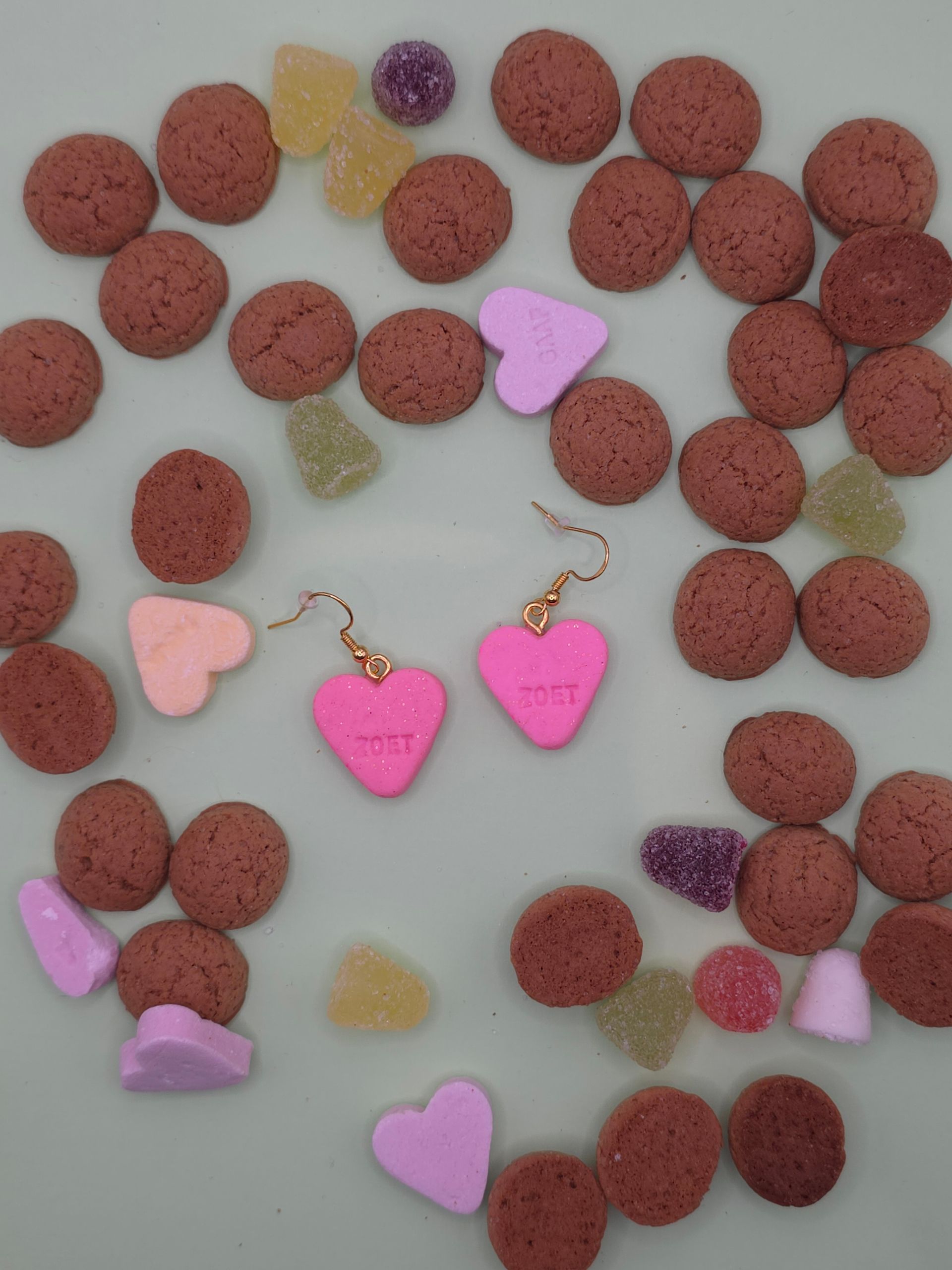 Roze hartvormige oorbellen en snoepachtige versieringen op een lichte achtergrond.