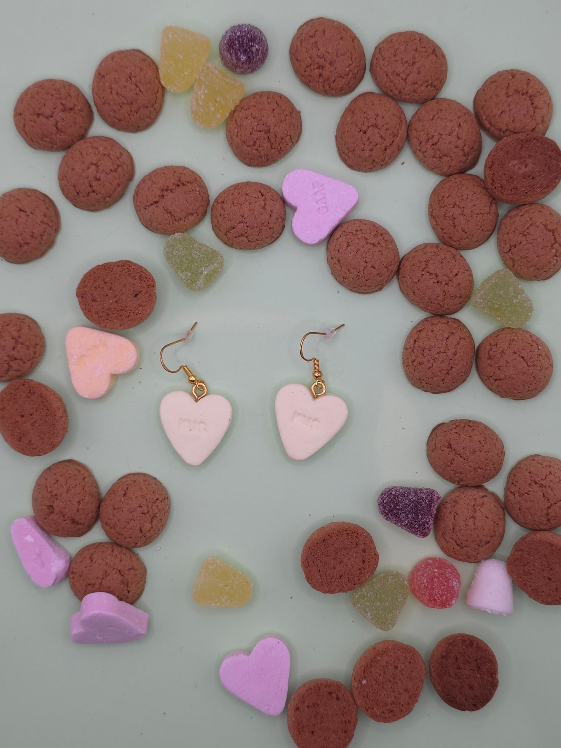 Hartvormige sieraden omringd door roodbruine kralen en pastelkleurige snoepstukjes op een witte achtergrond.