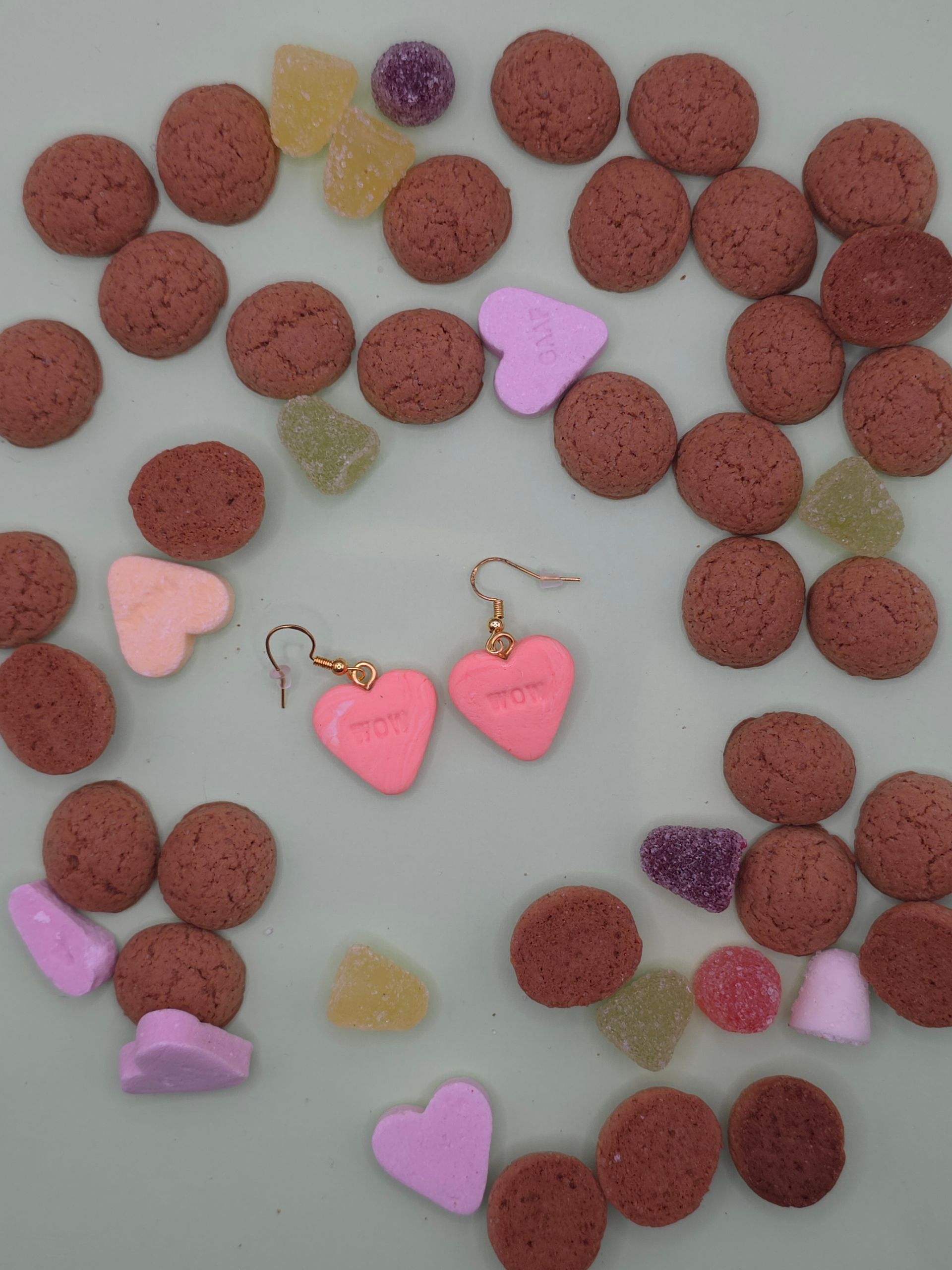 Hartvormig arrangement van rode en pastelkleurige snoepjes met twee roze hartvormige oorbellen in het midden.