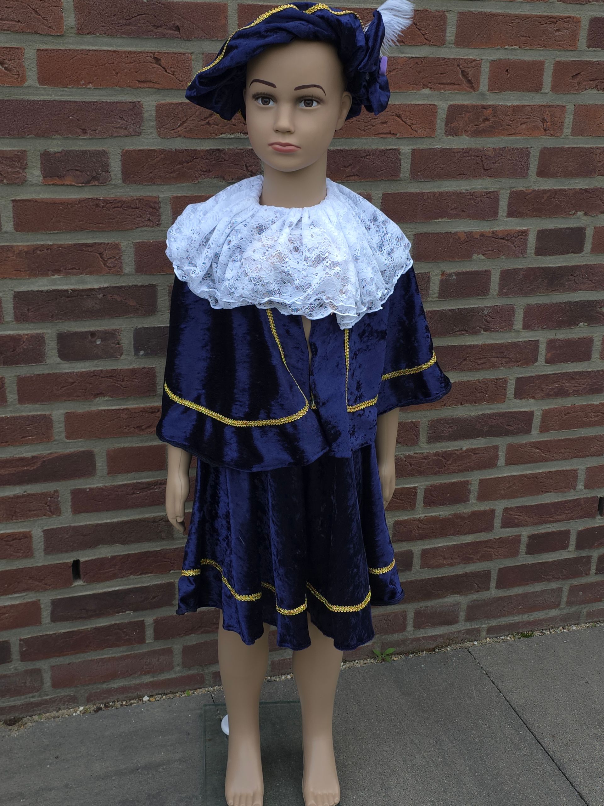 Mannequin wearing a dark blue ruffled dress with white lace collar, standing against a brick wall