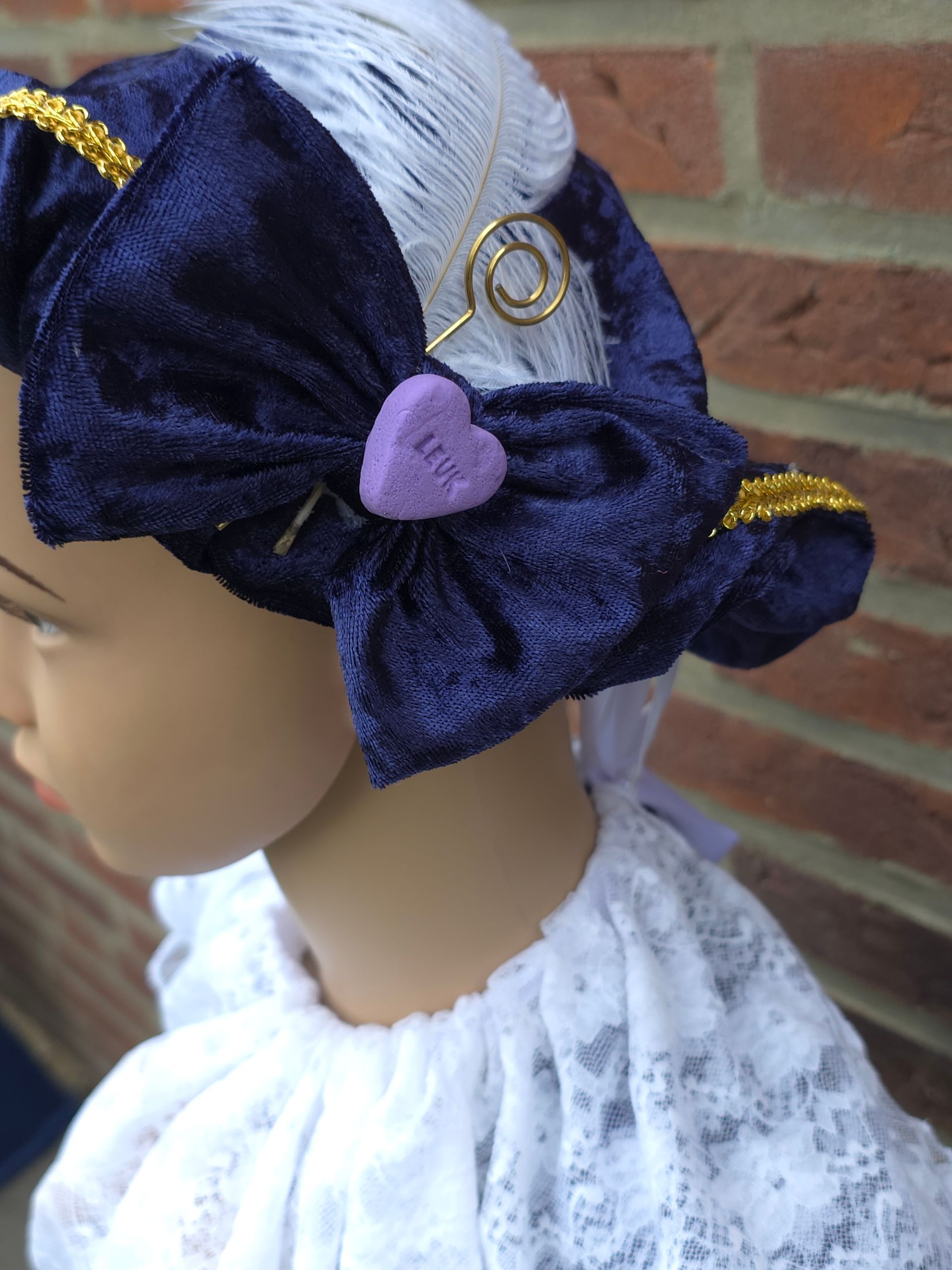 Profiel van een mannequin met een donkerblauwe fluwelen pietenmuts met lavendelkleurig hartornament en een witte kanten top.