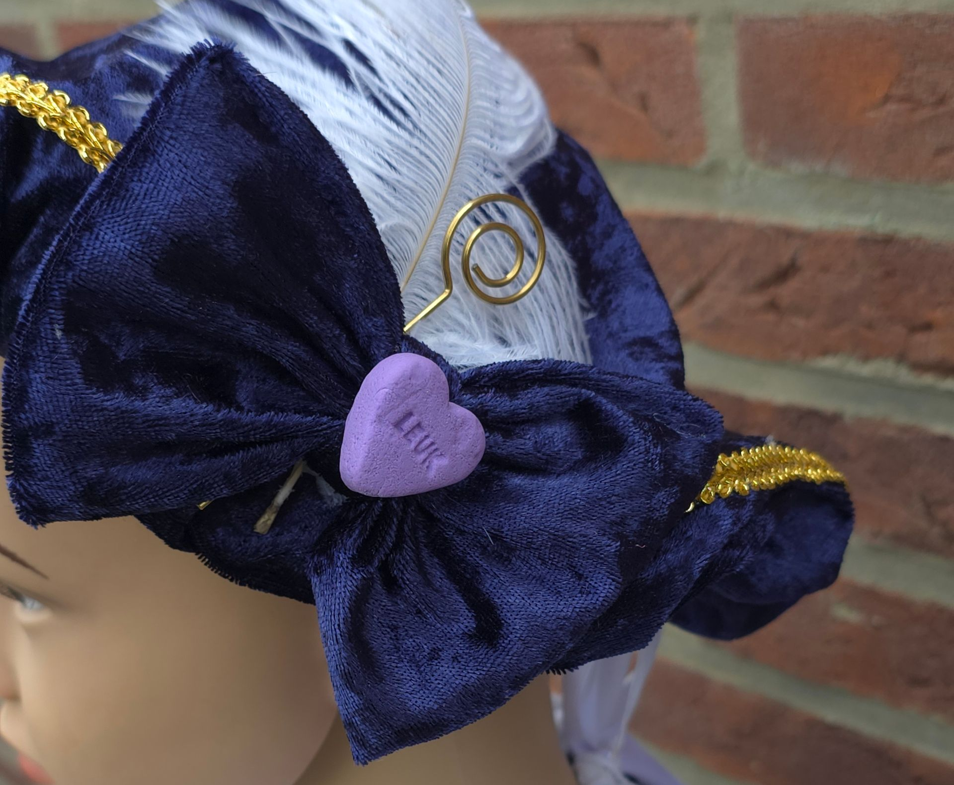 Een blauwe fluwelen strik met een paars hartje in het midden, geplaatst op zilverkleurig haar tegen een bakstenen muur.