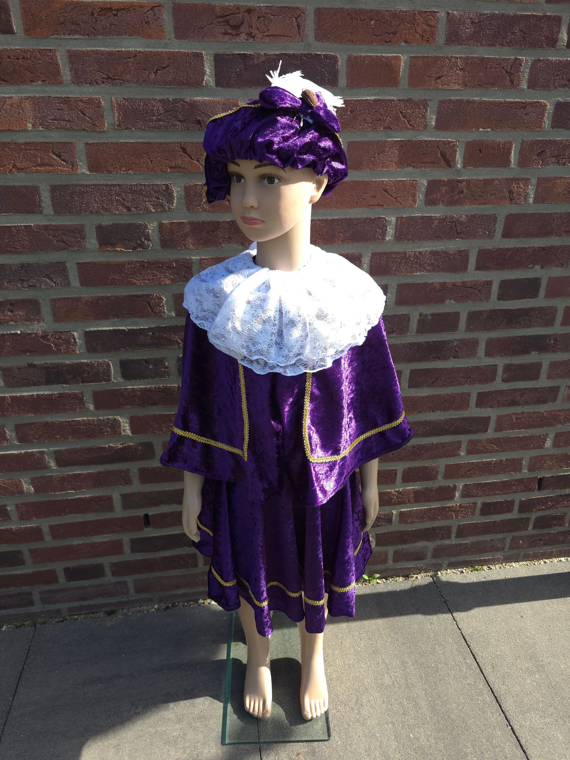Paarse pop met bijpassende hoed en outfit staat op de stoep tegen een bakstenen muur.