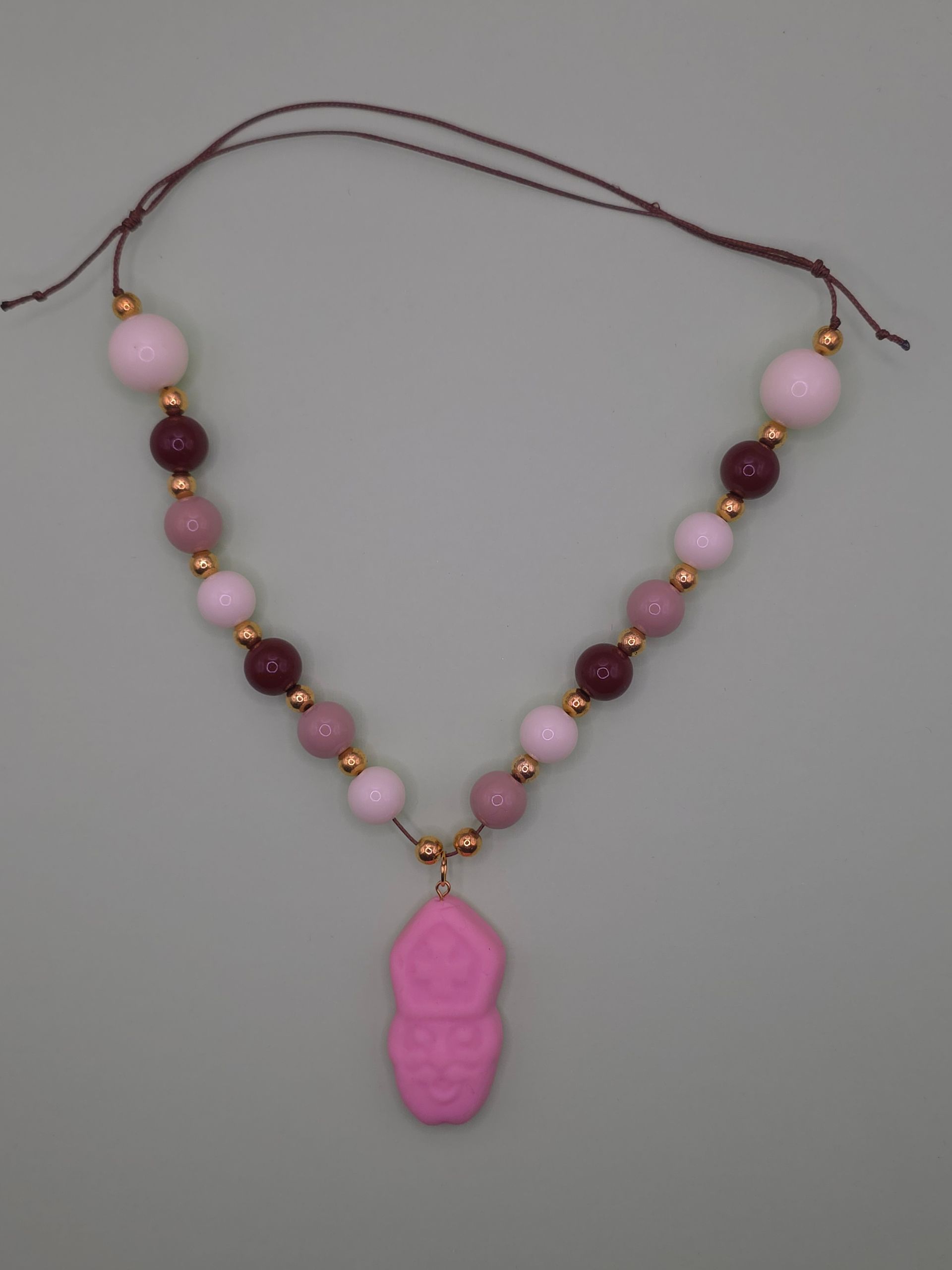 Roze hanger in de vorm van een poot aan een kralenketting met roze, bordeauxrode en gouden kralen.