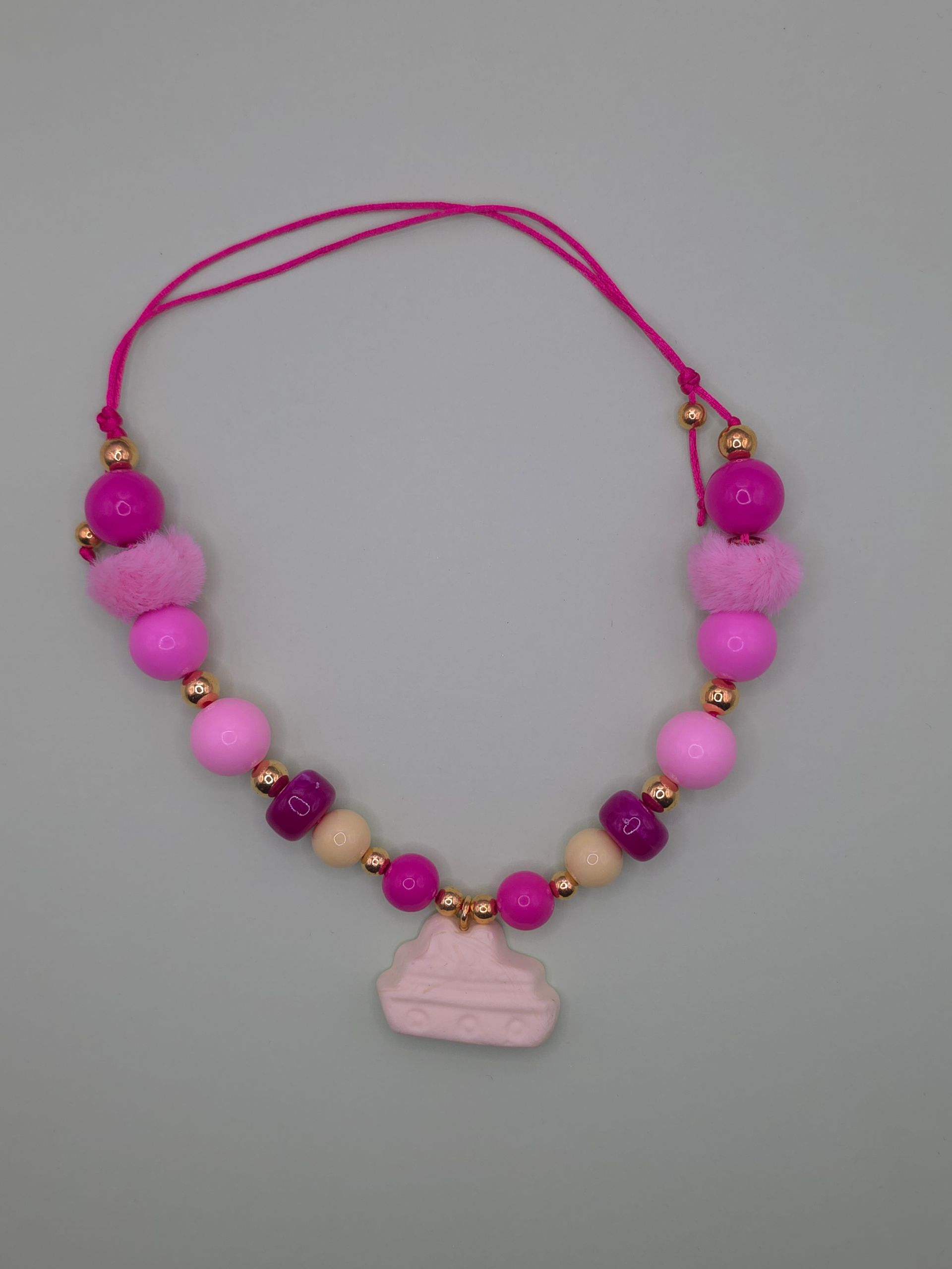 Roze kralenketting met een lichtroze hanger op een grijze achtergrond.