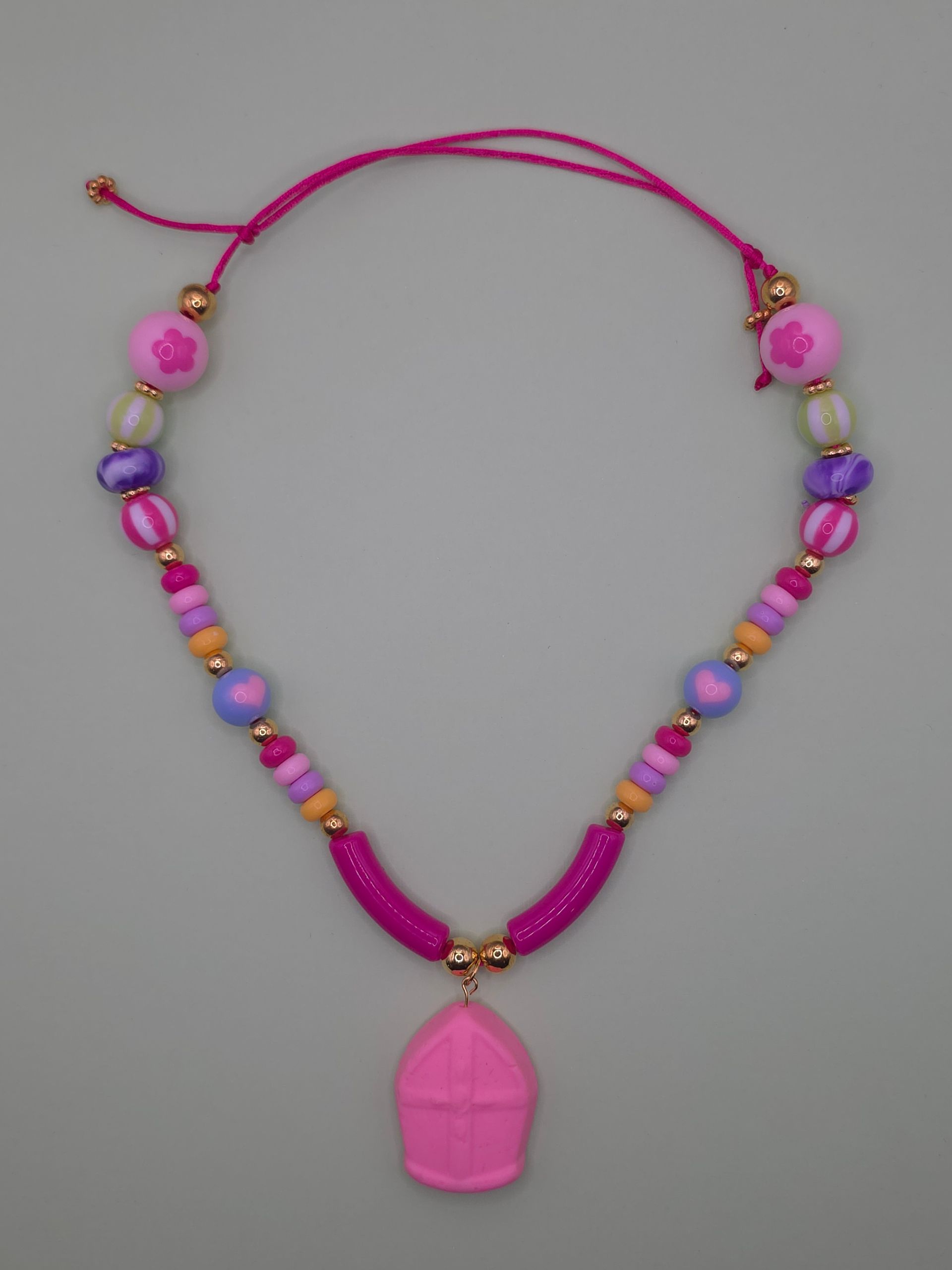 Roze kralenketting met een grote roze hanger op een grijze achtergrond.