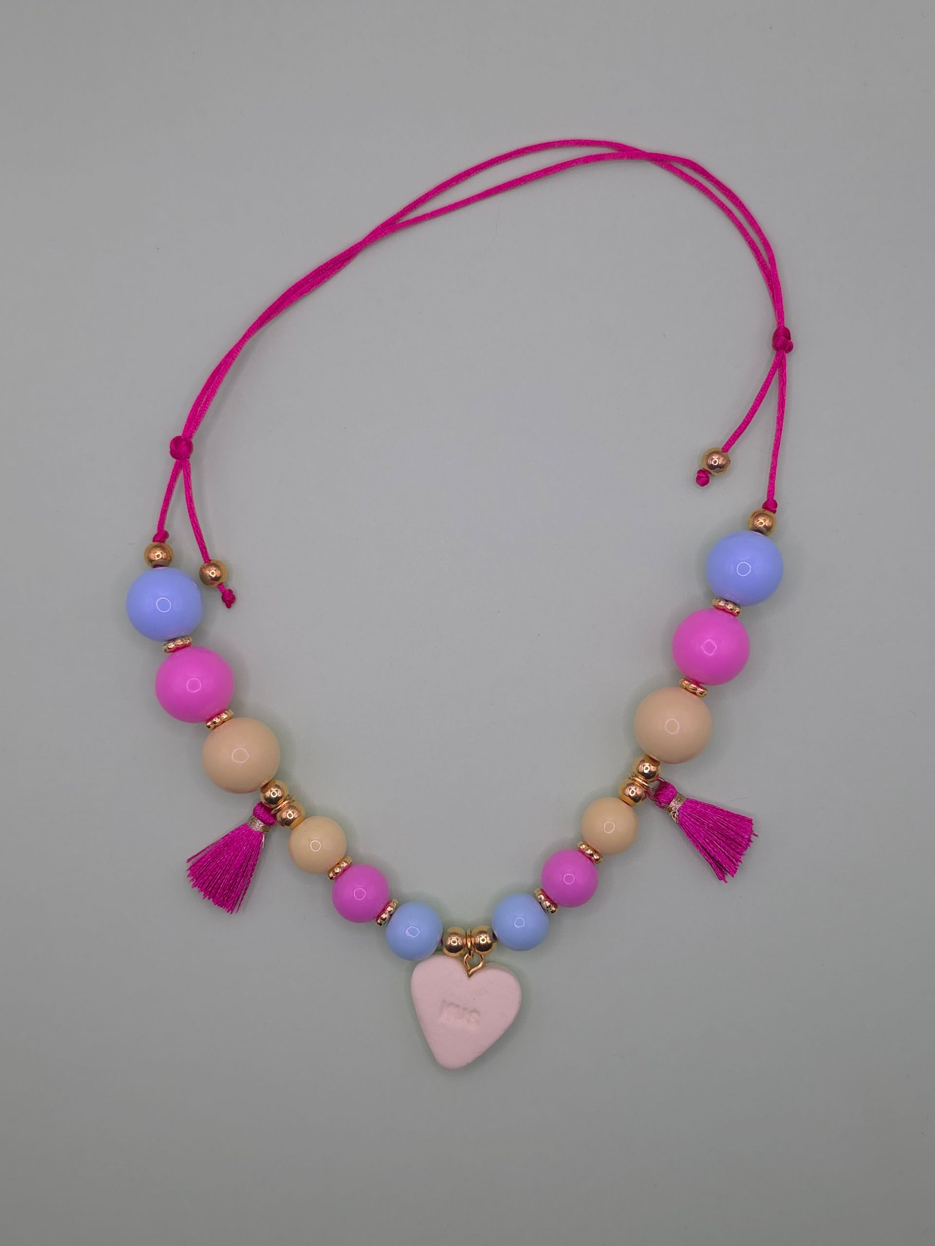 Roze kralenketting met hartvormige hanger en bungelende kwastjes op een witte achtergrond.